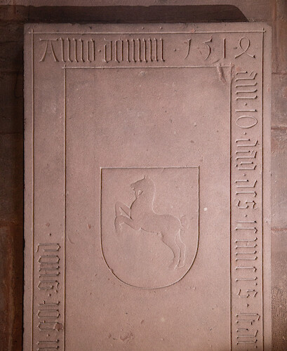 His tombstone with his coat of arms is located under the stained glass windows.